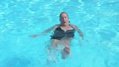 Güneşli yaz günlerinde temiz mavi havuzda geriye doğru yüzen mayolu olgun bir kadından.