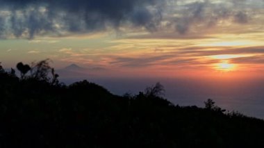 El Hierro Adası 'nın karanlık yüzeyi üzerinde bulutlarla kaplı renkli günbatımı gökyüzünün sağ tarafında, Teide arka planda.