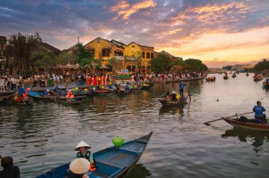 Tanımlanamayan insanlar teknede oturuyor ve bulutlu gün batımına karşı nehrin sakin sularında yüzüyorlar.