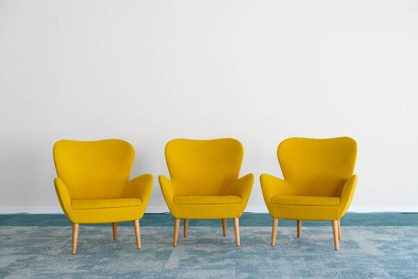 Классические желтые кресла с крепкими деревянными ножками, расположенными на пустом мраморном полу при дневном свете напротив стены.