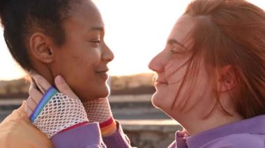 Gökkuşağı balık ağıyla kulağı delinen, siyah kız arkadaşlarının yüzlerine dokunan, rüzgarlı bir günde birbirlerini öpen ve burunlarını ovuşturan genç bir kadının gerçek zamanlı yan görüntüsü.