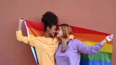 Lezbiyen çiftin, rüzgarlı bir günde burunlarını sarıp, LGBT bayrağına sarılıp nazikçe öpüştüğü ve siyahi bir kadının kız arkadaşının saçlarına dokunduğu gerçek bir zaman.