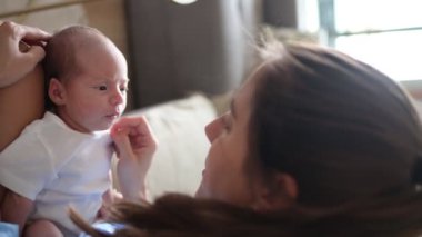 Neşeli bir annenin, evdeki hafif oturma odasında kanepede otururken yeni doğmuş şirin bir bebeğin yüzüne dokunduğu el kamerası görüntüsü.