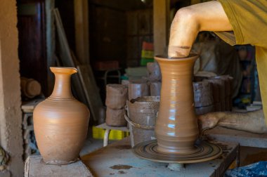 Ekin çömlekçisi atölyede çalışıyor ve el yapımı seramik vazo yaparken dönen çarkın üzerinde kil çömleği şekillendiriyor.