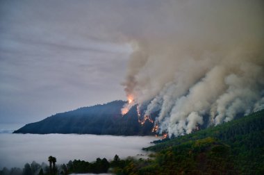 İspanya 'daki Kanarya Adaları' ndaki Tenerife 'de Orotava Vadisi yakınlarında volkanik volkan Teide ve akan lav ve duman bulutları ile resim gibi deniz manzarası.