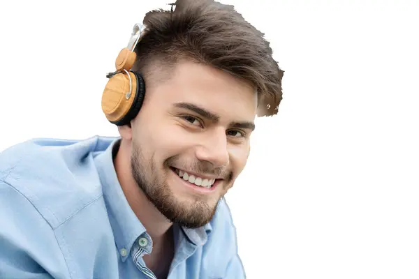Müzik dinlerken kameraya bakan ve beyaz arka planda izole edilmiş, kulaklıklı, gülümseyen sakallı genç bir erkek portresi.