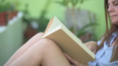 Kafede bulanık arka planda sandalyede otururken tanınmayan bir kadın kitap okuyor.