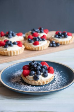 A vertical image of vanilla custard tarts topped with berries.