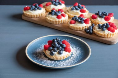 Blueberry and raspberry vanilla custard tarts on a blue table.