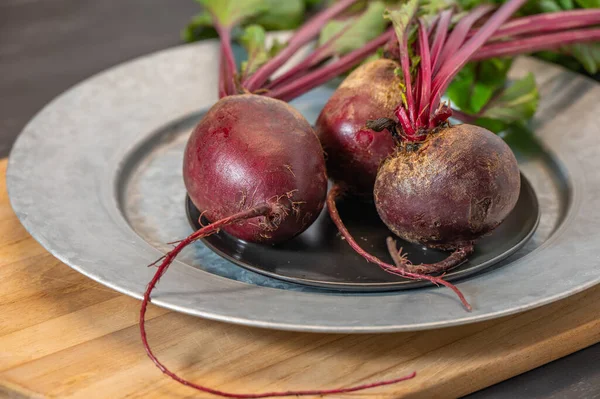 Three bright beets waiting on a platter before processing on a cutting board.