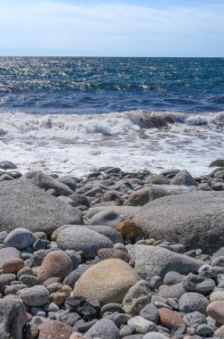 Norveç 'te güneşli bir yaz gününde büyük kayalar ve küçük çakıl taşlarından oluşan bir kıyı şeridine dalgalar çarpar..