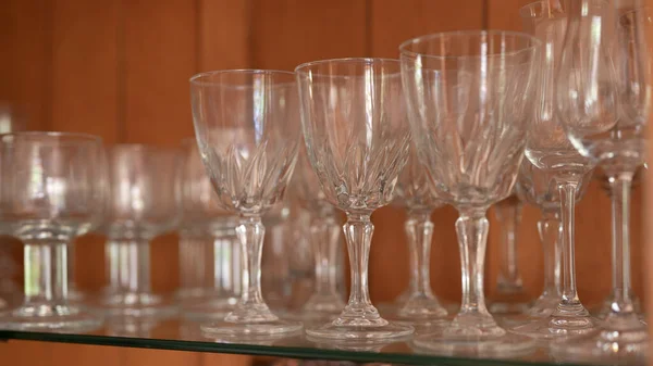 Rows of wine glasses lined up on the glass shelf of a china cabinet.