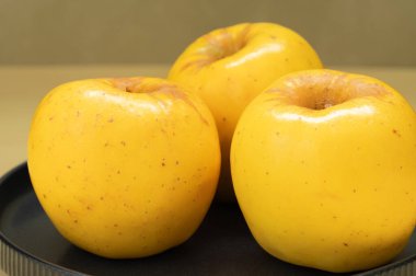 Gri bir tabakta üç sarı Opal elması.