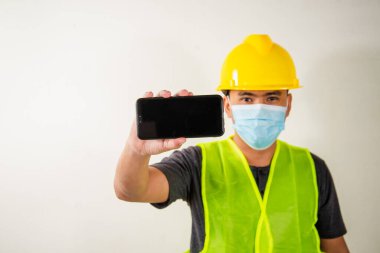 Tıbbi maskeli mühendis elinde akıllı telefon tutuyor..