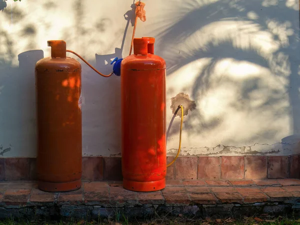 Two orange propane tanks against a wall illuminated by the light of the sunset, and the shadow of a palm tree, in a farm near the colonial town of Villa de Leyva in central Colombia.