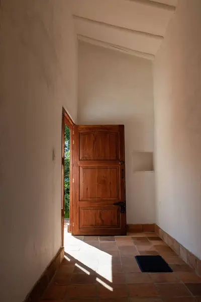 Hallway with an wooden open door and a small rug, illuminated by the morning sun, in a farmhouse at the eastern Andes mountains of central Colombia.