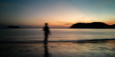 Gündoğumu sahili ve siyah siluet insanlar hareket bulanıklığı. Doğa arkaplan denizi, altın akşam gökyüzü ve bulanık ada.