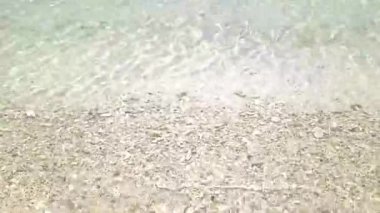 4K gerçek zamanlı video kaydı. Açık deniz dalgaları sıcak ve güneşli bir öğleden sonra sahilde nazikçe dalgalanır..