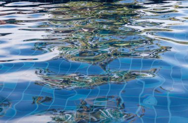 Mavi yüzme havuzu suyu, dalgalar ve güneş ışığı yansımaları.