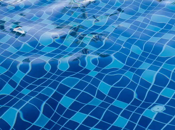 Mavi yüzme havuzu suyu, dalgalar ve güneş ışığı yansımaları.