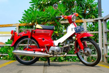 Otomotiv fotoğrafçılığı. Klasik Honda Super Cub C90 Super Deluxe kırmızı ve beyaz Endonezya Bandung 'da bir alışveriş merkezinin çatısına park edilmiş.