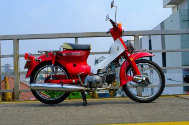 Otomotiv fotoğrafçılığı. Klasik Honda Super Cub C90 Super Deluxe kırmızı ve beyaz Endonezya Bandung 'da bir alışveriş merkezinin çatısına park edilmiş.