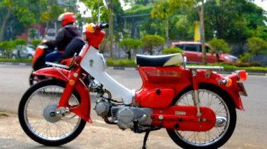 Klasik motosiklet görüntüsü. 1975 C90 Super Cup motorsikletinin trafik dolu yoğun bir yolun kenarına park edildiği zaman dilimi videosu. Bandung - Endonezya