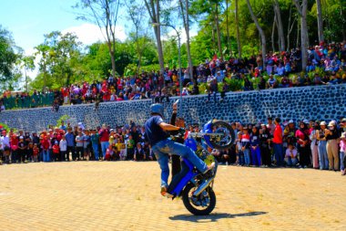 Bandung, Batı Java, Endonezya - 17 Ağustos 2023: Bir dublör Endonezya 'nın 78. bağımsızlık günü festivalinde motosiklet kullanarak serbest gösteri yapıyor, canlı bir kalabalıkla performans sergiliyor.