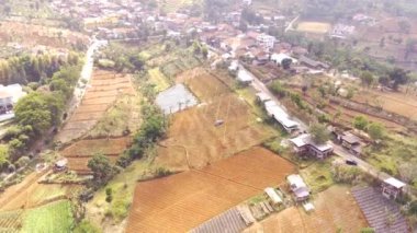 Bandung City, Endonezya 'daki çiftlik arazilerinin ve yerleşim yerlerinin hava manzarası videosu. Drone Tarımsal Alanlar ve Yerleşimlerin İnsansız Hava Aracı. Dağın tepesinde 4K video