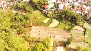 Drone Videoları. Hiper Lapse Görüntüleri. Majalaya kırsalının kuş bakışı görüntüsü. Yeşil pirinç tarlaları, yerleşim bölgeleri ve yerleşim yerleri var. Uçan bir drondan havadan ateş edilmiş. Endonezya 
