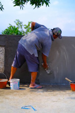 Bandung, Batı Java, Endonezya - 27 Aralık 2023: Sanayi Fotoğrafçılığı. Gri gömlekli adam duvarlara sıva yapıyor. Duvarı çimento havanıyla kaplamak..