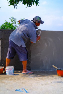 Bandung, Batı Java, Endonezya - 27 Aralık 2023: Sanayi Fotoğrafçılığı. Gri gömlekli adam duvarlara sıva yapıyor. Duvarı çimento havanıyla kaplamak..