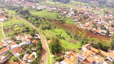 Drone Görüntüleri. Batı Java Eyaleti, Endonezya 'daki uzun tren yolunun havadan görüntüsü. Yerleşim alanlarını, pirinç tarlalarını, tarlaları ve dağları geçen tren yolu. 4K 30fps çözünürlüklü İHA 'dan video görüntüsü