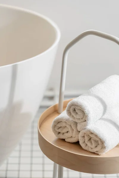 Clean and soft terry towels on the small wooden table near wash basin. Bathroom with personal accessory in hotel room. Fresh cloth near tub, close up view