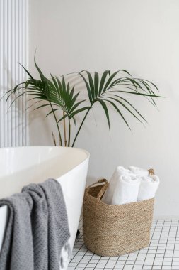 Hasır sepetin içinde beyaz rulo havlular, modern banyonun küvetinin yanındaki saksıda saksıda saksıda duruyor. Otel odasında nesne kavramları. Minimalist tarzda tasarlanmış yeni bir daire.