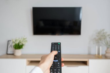Kadın eli TV kumandası ve televizyon açmak için düğmeye basmak, rahat bir apartmanın oturma odasında koltukta oturmak, eğlenmek ve evde dinlenmek için.