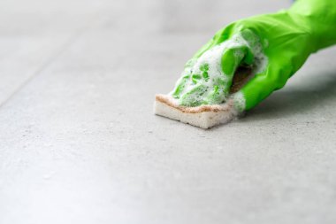 Kadın eli yeşil plastik eldiven içinde yer döşemesini sabun köpüğü ve süngerle yıkıyor daire odasında, kırpılmış atış, temizlik servisi konsepti