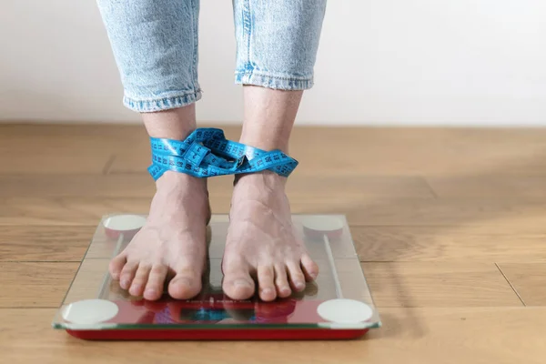 stock image Cropped shot of young barefoot woman standing on glass flooring scales with tied feet, checking her weight. Female obsessed with idea of slimming, suffering from eating disorder