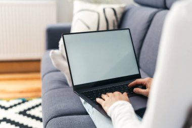 Kırpılmış kadın eli görüntüleri dizüstü bilgisayar ekranı, klavye ve oturma odasındaki kanepede iletişim kurma.