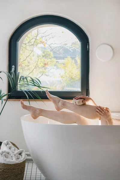 健美和日常美感的概念 在酒店房间里 一个温柔的女人在洗澡 雌性动物抬起脚 用海绵洗她美丽的腿 做护肤工作 — 图库照片