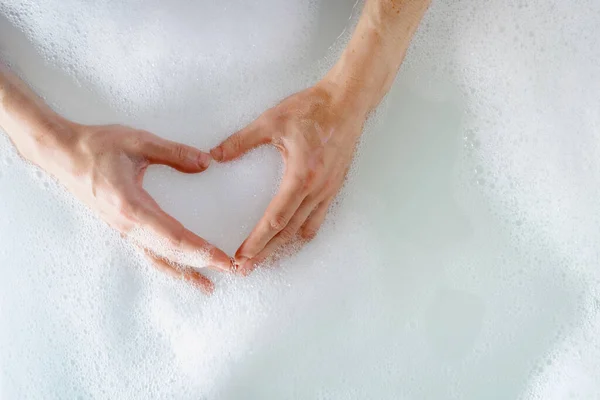 Beauty routine and self care procedure concepts. Top view of woman taking bath, hold hands in hot bubble water, making heart shape and showing love gesture