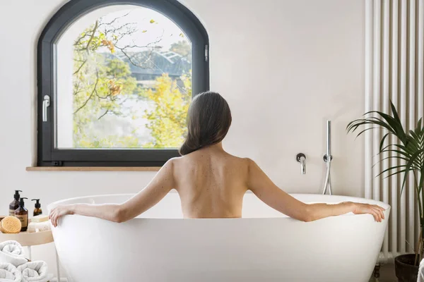 后视镜 年轻女子洗澡 在酒店浴室度过上午 看窗户 漂亮无忧无虑的女人坐在现代公寓房间的浴缸里 — 图库照片