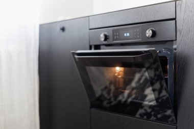 Çağdaş mutfakta siyah ahşap dolapta bulunan elektrikli fırında açık kapı ve ışık üzerine seçici bir odak.