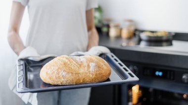 Havluyla kadın ellerine yakın çekim ve mutfak arka planında çıtır çıtır ekmek ve taze ev yapımı ekmek örtüsü.