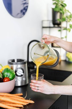 Kadın elleri elektrikli blender içinde meyve ya da sebze suyu hazırlıyor ve ev mutfağında bardağa içki dolduruyor. Kırpılmış iğne, sağlıklı beslenme konsepti.