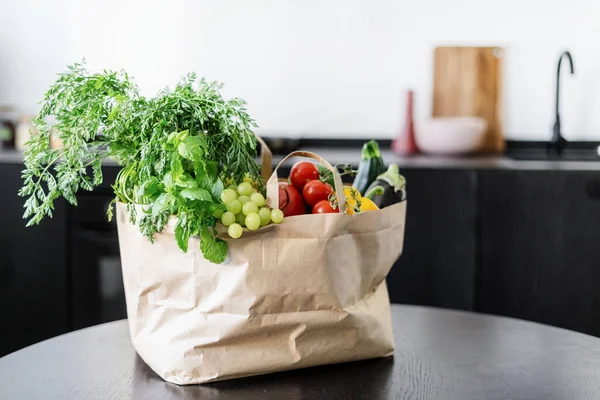 full paper bag with fresh vegetables, fruits and herbs at home kitchen with blurred background, vegetarian diet, grocery purchase and delivery concept