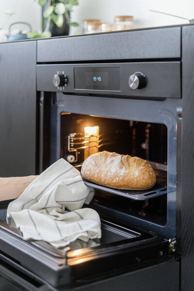 приготовление пищи дома, обрезанный снимок женской руки с полотенцем вынимая домашний хлеб буханка на поднос из плиты, современная техника