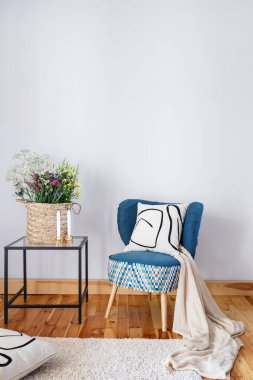 Dairesinde rahat bir iç mekan, yastıklı ve ekoseli mavi koltuk, hasır sepetli çiçekler ve cam sehpada mumlar ve ahşap zeminde halı.