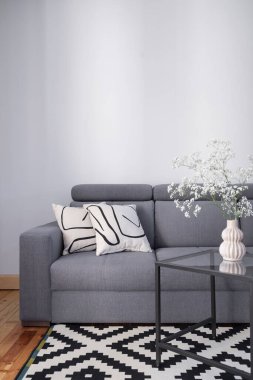 Yastıklı rahat bir kanepe, cam sehpada çiçekli seramik vazo ve modern iç mimarisi olan ahşap döşeme.