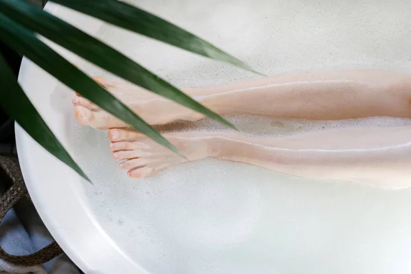 割下的女性腿照片 俯瞰躺在浴室浴缸里的女人 浴缸里有温水和泡泡 去毛化 去毛化 护肤概念 女孩在热带酒店洗澡 享受温泉疗程 — 图库照片